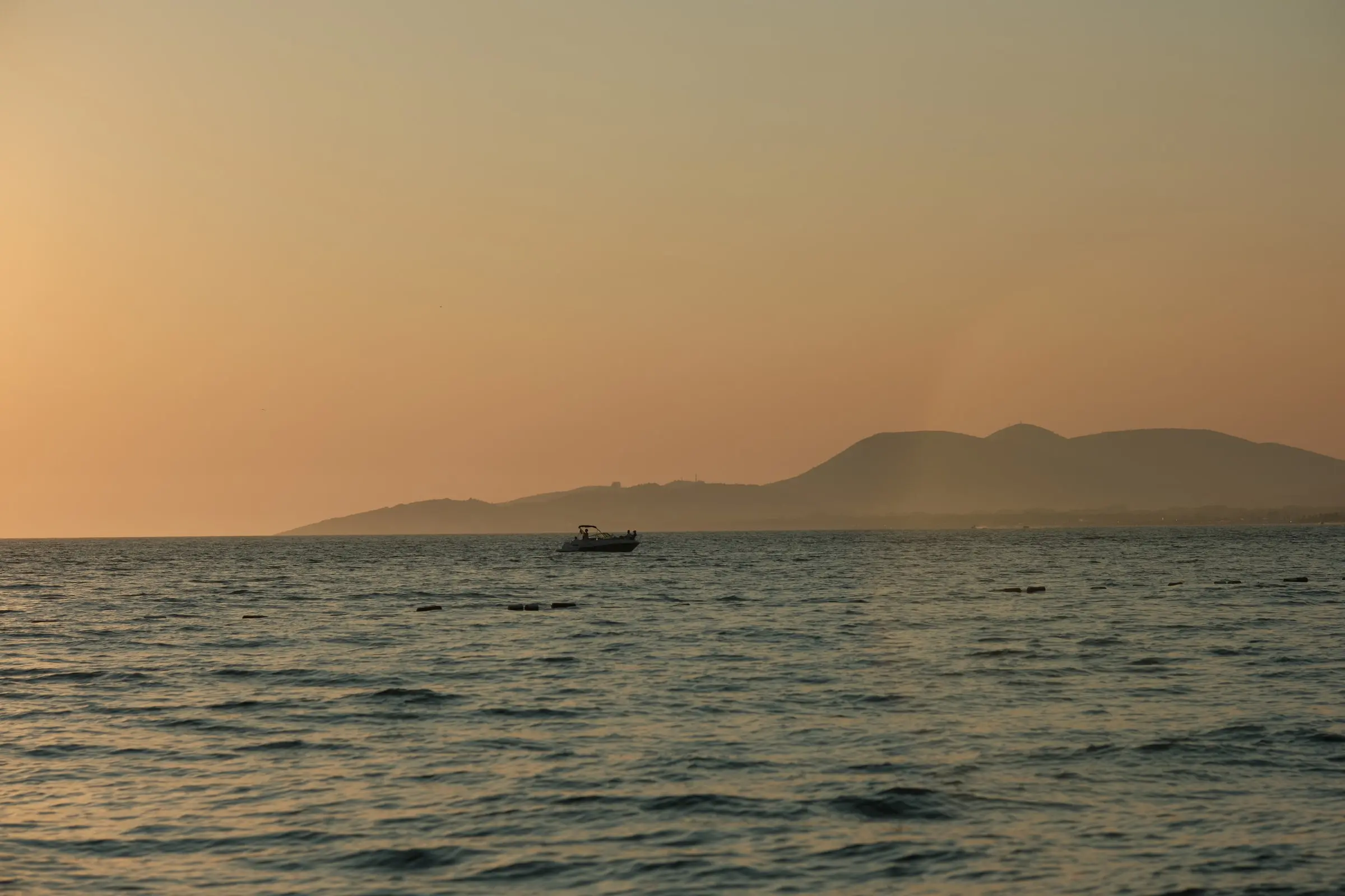 Gliser na otvorenom moru u zalasku sunca, a na horizontu brda u izmaglici